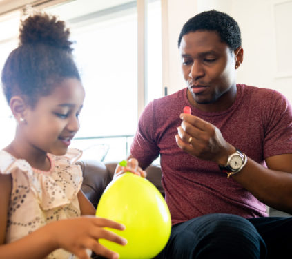 Portrait of a daughter and father having fun together and playing with balloons at home. Monoparental concept.